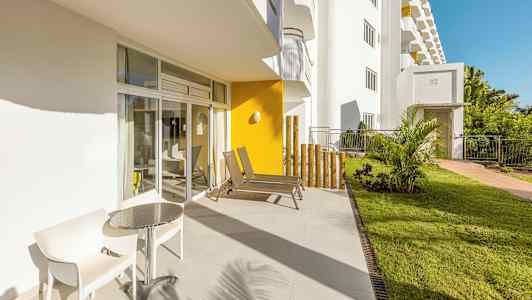 En solig terrass med två stolar och ett bord bredvid glasdörrar. (AI-genererad text)