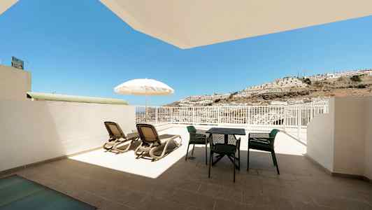 En terrass med solstolar, parasoll och utemöbler, med utsikt mot solen och en bergskulle. (AI-genererad text)