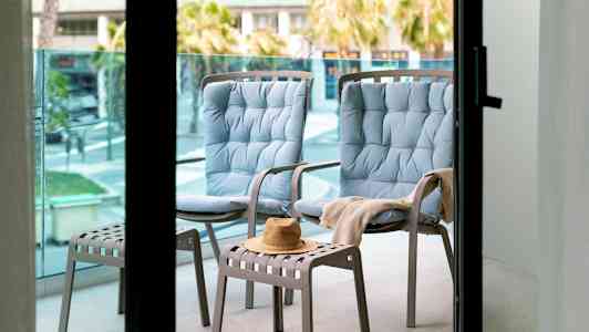 Två blåa sittstolar och en pall med en hatt på en balkong. (AI-genererad text)