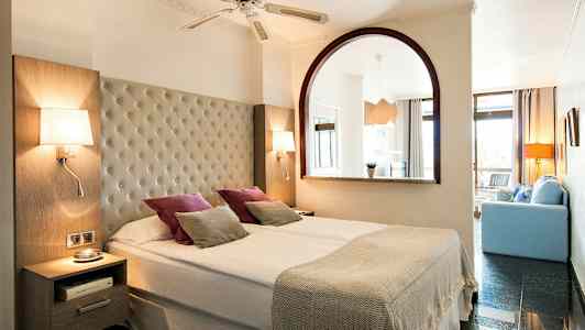 Dubbelrum med bred säng, lampor och dekorativa kuddar. (AI-genererad text)