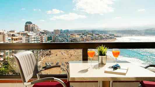 En balkong med bord och stolar, utsikt över en strand och stad. (AI-genererad text)