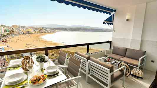 Ett möblerat balkongområde med utsikt över en strand och hav. (AI-genererad text)