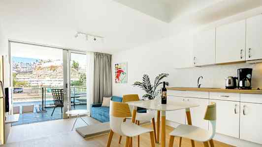 Ljust möblerat hotellrum med köksdel och balkong med utsikt. (AI-genererad text)