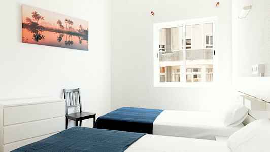 Två enkelsängar i ett ljust rum med en blå filt på varje säng. (AI-genererad text)