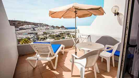 En terrass med solsängar, bord och stolar samt utsikt över havet och byggnader. (AI-genererad text)
