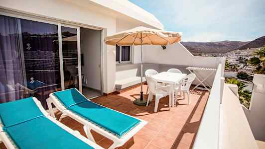 En terrass med två solstolar, ett möblemang med parasoll och utsikt över en stad och berg i fjärran. (AI-genererad text)