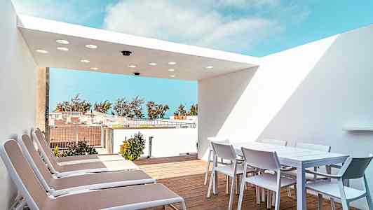 Terrass med solstolar och ett matbord med stolar under en vit taköverbyggnad. (AI-genererad text)