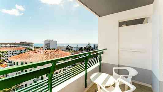 Balkong med bord och stolar samt utsikt över byggnader och havet. (AI-genererad text)