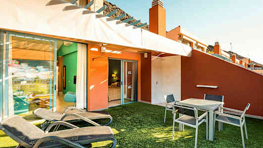 En terrass med solstolar, bord och stolar samt utsikt in mot ett sovrum. (AI-genererad text)