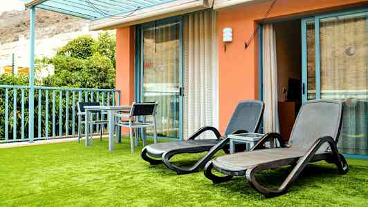 En terrass med solstolar och ett bord med stolar, samt grön konstgjord gräsmatta. (AI-genererad text)
