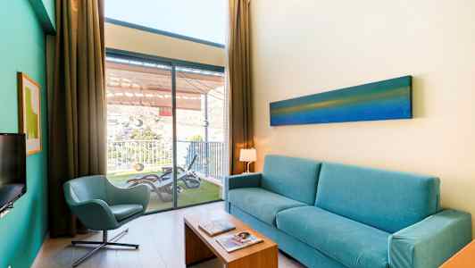 Vardagsrum med blå soffa, stol och utsikt ut mot en balkong. (AI-genererad text)