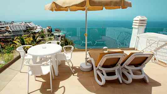 Solterrass med bord, stolar och solstolar samt havsutsikt. (AI-genererad text)