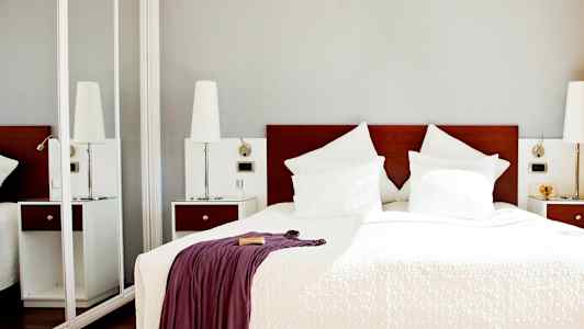 Ett hotellrum med en dubbelsäng som har vita lakan och kuddar samt ett täcke med en draperad filt. (AI-genererad text)