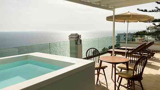 Terrass med en liten pool, bord och stolar samt solstolar med utsikt över havet. (AI-genererad text)