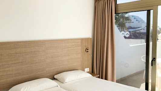 Två enkelsängar med vita lakan bredvid en glasdörr med utsikt. (AI-genererad text)