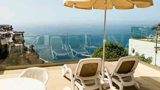 Två solstolar med en parasoll på en terrass med havsutsikt. (AI-genererad text)