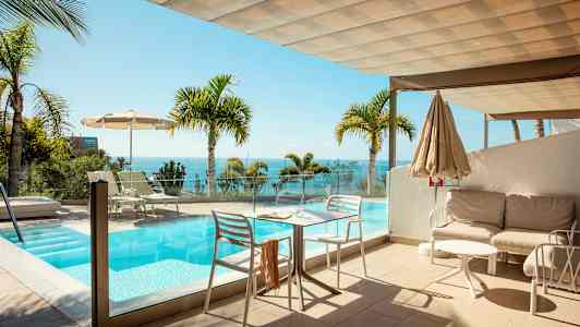 En uteplats med en pool och utsikt över havet, omgiven av palmträd. (AI-genererad text)