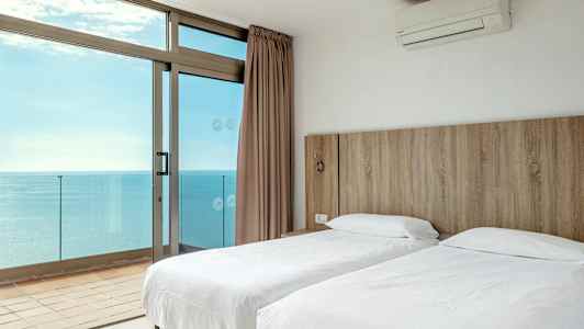 Ett hotellrum med två enkelsängar och utsikt över havet genom stora fönster. (AI-genererad text)