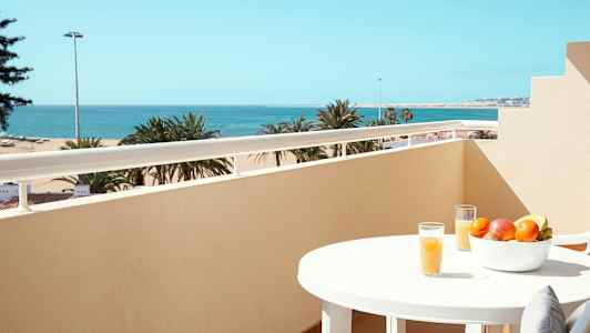 Balkong med havsutsikt, ett bord med fruktskål och glas med juice. (AI-genererad text)