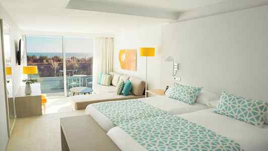 Ljusa hotellrum med dubbelsäng, sittgrupp och balkong med havsutsikt. (AI-genererad text)