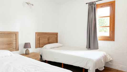 Ett rum med två enkelsängar, trädetaljer och ett fönster med grå gardiner. (AI-genererad text)