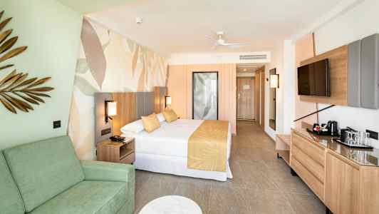 Hotellrum med säng, soffa och TV. Inredning i ljusa färger. (AI-genererad text)