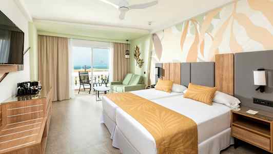 Hotellrum med två enkelbäddar och en balkong som har utsikt över havet. (AI-genererad text)