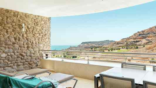 Terrass med solstolar och utsikt över havet och en bergig landskap. (AI-genererad text)