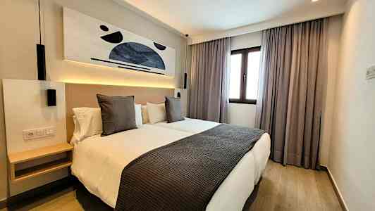 Ett modernt hotellrum med två enkelsängar, konst på väggen och ett fönster med gardiner. (AI-genererad text)