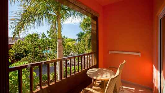 Balkong med två flätade stolar och bord, omgiven av växter och palmer. (AI-genererad text)