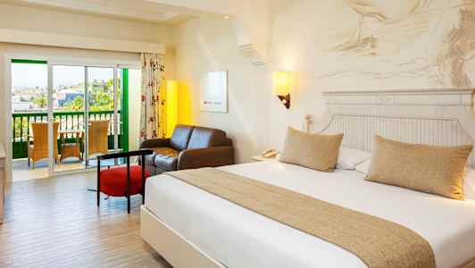 Ett hotellrum med en dubbelsäng, en sittgrupp och en balkong. (AI-genererad text)