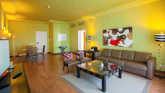 Vardagsrum med en grön vägg, brun soffa, konst på väggen och ett matbord med stolar. (AI-genererad text)