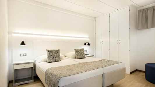 Dubbelrum med vita väggar, dubbelsäng, sänglampor och garderob. (AI-genererad text)