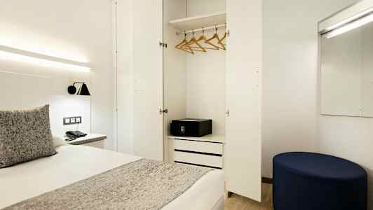 En hotellrum med öppen garderob, säng, och spegel. (AI-genererad text)