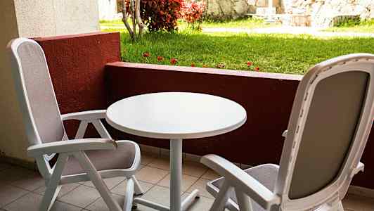 Två sittplatser med bord på en balkong med utsikt mot gräsmatta och stenmur. (AI-genererad text)