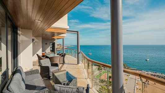 En balkong med sittmöbler och utsikt över havet och stranden. (AI-genererad text)