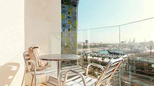 En balkong med två stolar och bord, med utsikt över hamnen. (AI-genererad text)