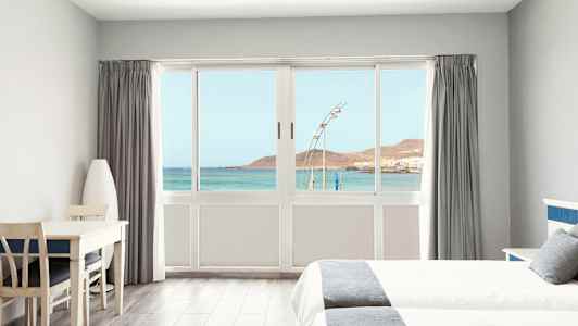 Ljust hotellrum med utsikt över havet genom en stor fönsterfront. (AI-genererad text)