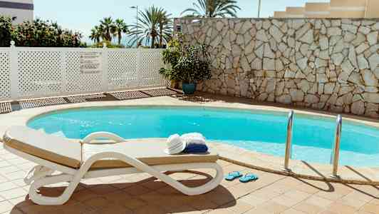 Utomhuspool med solsäng och en stapel handdukar och hatt. (AI-genererad text)