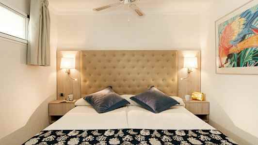 Ett hotellrum med en dubbelsäng, stoppad sänggavel, takfläkt, och vägglampor. (AI-genererad text)