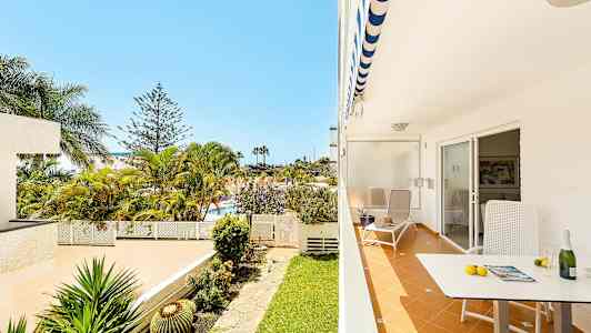 En uteplats med stol och bord, utsikt över en trädgård och palmträd. (AI-genererad text)