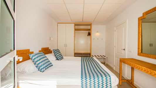 Ett hotellrum med en säng, sängkläder och en spegel. (AI-genererad text)