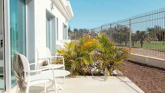 Terrass med vita stolar och bord, omgiven av grön vegetation och staket. (AI-genererad text)