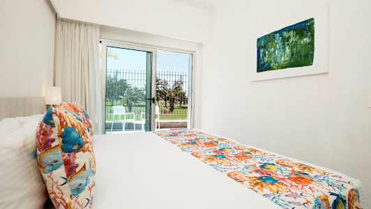 Ett ljust hotellrum med en säng, färgglada dekorationer och en öppning till en uteplats. (AI-genererad text)
