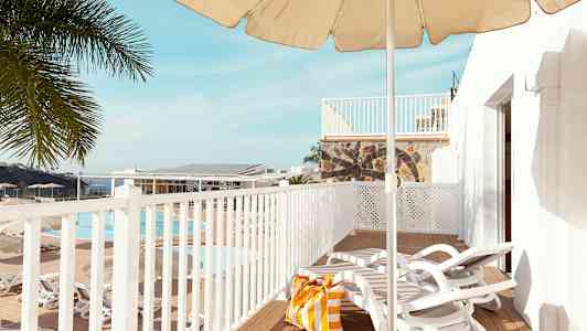 Vy över en terrass med solstolar, parasoll och en strandväska. I bakgrunden syns en pool och palmer. (AI-genererad text)