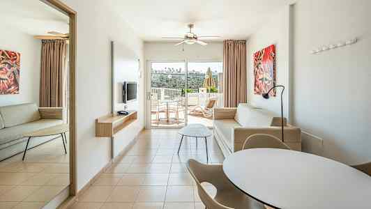 Ett modernt hotellrum med två soffor, matbord och stolar samt en balkong med utsikt. (AI-genererad text)