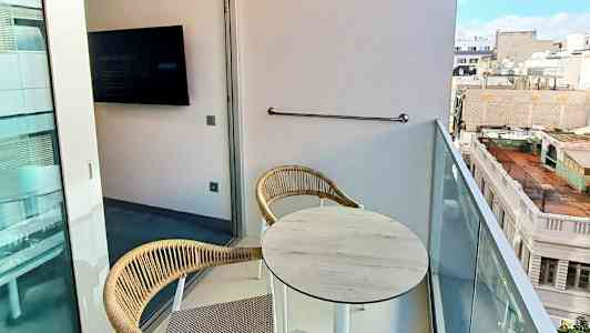 Bild på en balkong med två stolar och ett bord samt utsikt över stadens byggnader. (AI-genererad text)