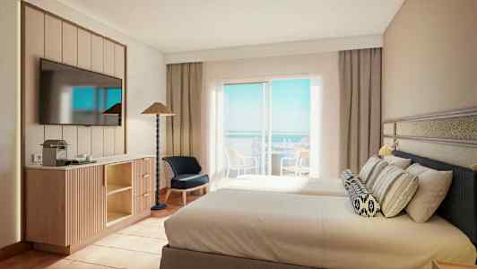 Ett hotellrum med två sängar, en platt-TV på väggen, möbler och en balkong med utsikt över havet. (AI-genererad text)