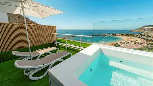 Terrass med solsängar, parasoll och liten pool med utsikt över strand och hav. (AI-genererad text)