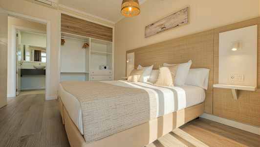 Ett ljust sovrum med en dubbelsäng, garderob och öppet badrum. (AI-genererad text)